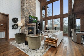 A spacious living room with a stone fireplace, large windows, and a cozy seating area. - Blue Fox Lodge - Pet Friendly (Blue Ridge)