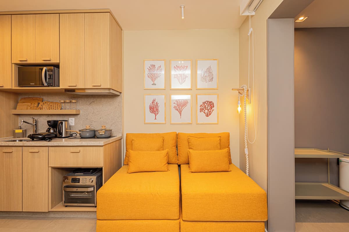 A compact living space with a kitchenette, a bed with two yellow pillows, and six framed wall art pieces.