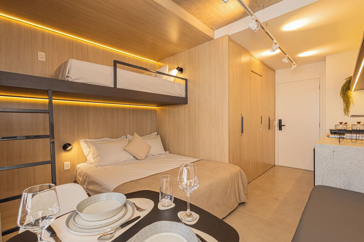 A compact hotel room with a bunk bed, a dining table set with plates and glasses, and a kitchenette area.