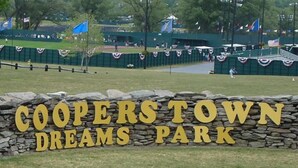 A sign for Cooper's Town Dreams Park with a stone wall and grass in the foreground.