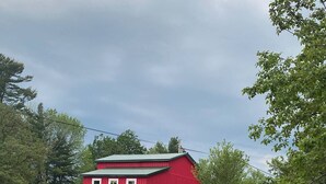 A red barn with a dirt path leading to it, surrounded by trees and greenery.