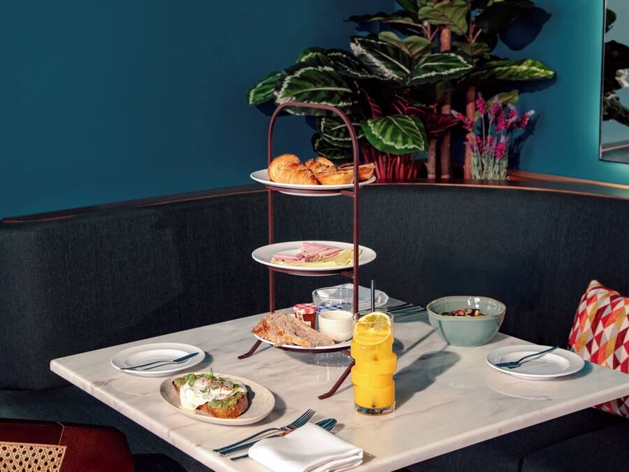 A dining area with a table set for breakfast, including croissants, a fruit drink, and various dishes.