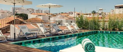 A rooftop pool area with lounge chairs and umbrellas, surrounded by city buildings.