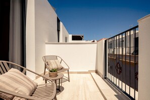 Un balcon avec une chaise, une petite table ornée d’une plante et une rambarde.
