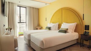 A hotel room with two beds, a desk, a chair, a bedside table with a phone, and a window with curtains. - The MN56 Hotel (Lagos)