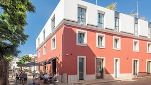 A red building with multiple windows and doors, outdoor seating area with tables and chairs, and a cobblestone street. - The MN56 Hotel (Lagos)