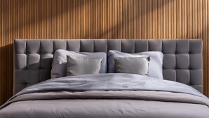 Ein modernes Schlafzimmer mit einer karrierten Kopfteil, grauer Bettwäsche und einer Wand aus Holzlamellen.