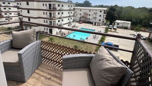 Un balcón con mobiliario de mimbre y vistas a una zona de piscina rodeada de edificios.