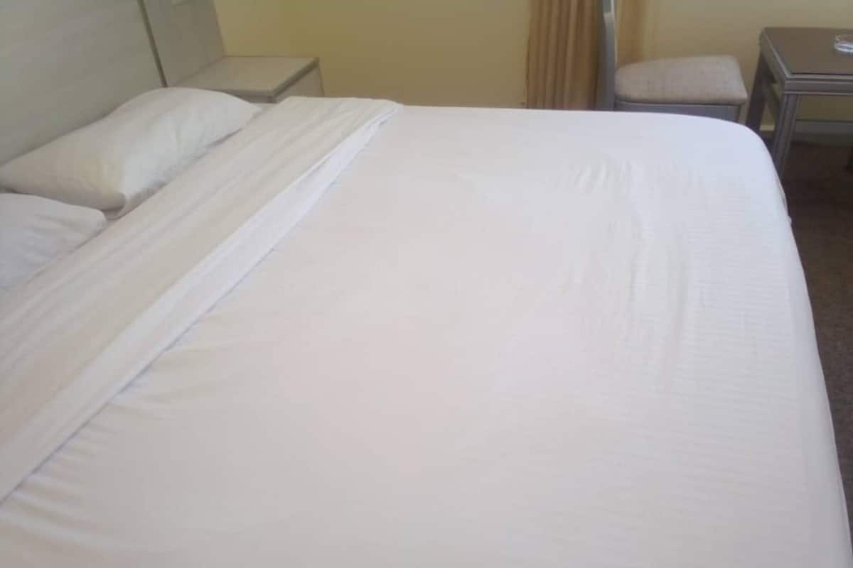 A neatly made bed in a hotel room with a headboard, a small bedside table, and a chair.