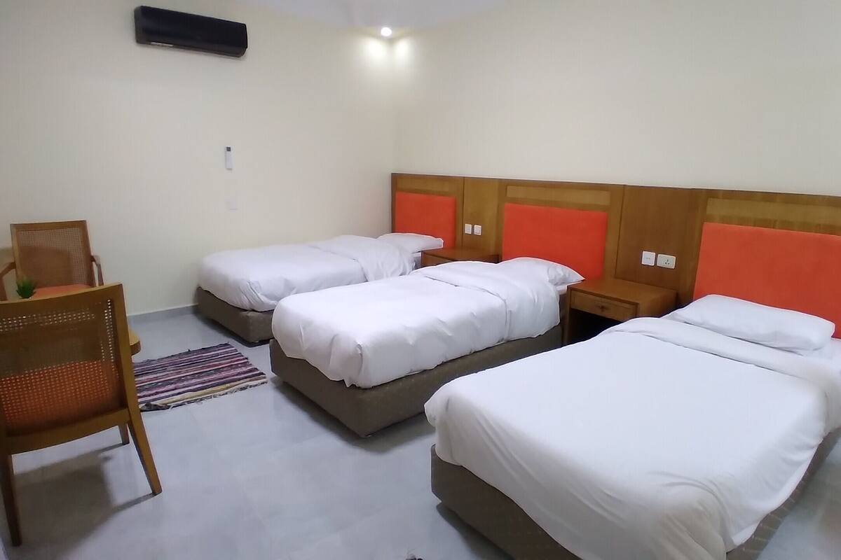 A hotel room with three beds, a chair, and a small table.