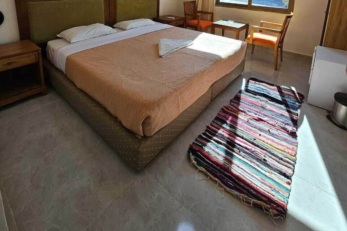 A hotel room with a large bed, a small table, a chair, a window with curtains, and a ceiling light.