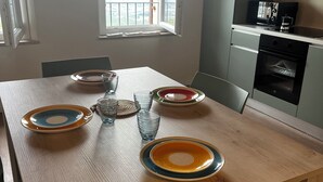 A dining table with plates and glasses, a window with a view, and a kitchen area with appliances. - Casa Vacanze Conca D'Oro (San Giorgio di Valpolicella)