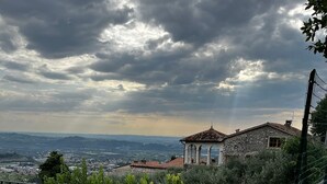 A terrace with a table and chairs, a large terracotta pot, and a view of a town and hills under a cloudy sky. - Casa Vacanze Conca D'Oro (San Giorgio di Valpolicella)
