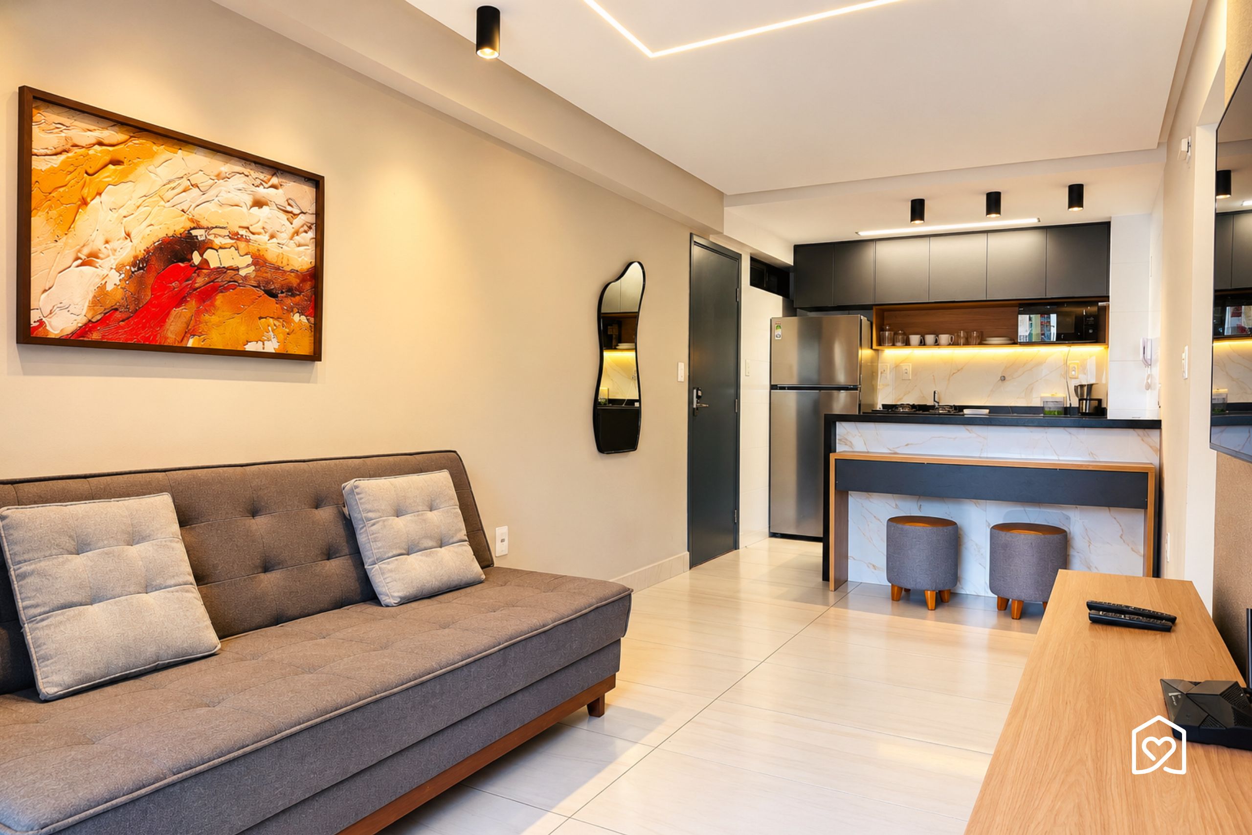 Uma sala de estar moderna com sofá cinza, uma pintura abstrata grande e uma cozinha com armários escuros e uma geladeira de aço inoxidável.