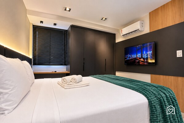 A modern hotel room with a bed, a flat-screen TV, and a cityscape view. - Mardisa Design - LikeHome Hospedagens (João Pessoa)