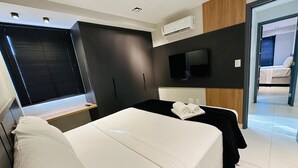 Ein modernes Hotelzimmer mit Bett, Fernseher, Klimaanlage und Blick auf das Nachbarzimmer.