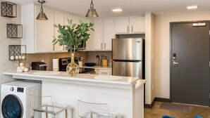 A modern kitchen with white cabinets, stainless steel appliances, and a central island with bar stools. - The Groovy Blue Skyview (Birmingham)