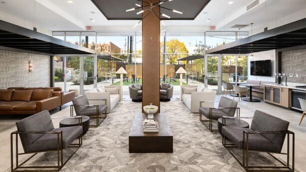 A spacious indoor area with a central column, multiple seating arrangements, and a kitchen area visible through glass walls. - The Groovy Blue Skyview (Birmingham)