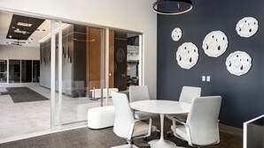 A modern conference room with a round table and white chairs, a dark accent wall with abstract art, and a glass partition separating the room from another space. - The Groovy Blue Skyview (Birmingham)