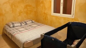 Une chambre à coucher avec un lit, un berceau, une fenêtre avec des rideaux et un luminaire.