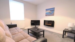 Ein Wohnzimmer mit einer Couch, zwei Flachbildfernsehern, einem Kamin und einem Gemälde an der Wand.