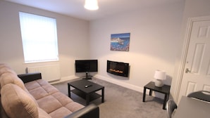 A living room with a sofa, a coffee table, a flat-screen TV, a fireplace, and a painting on the wall. - Fishermans View Summa (Fleetwood)