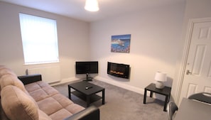 A living room with a sofa, a coffee table, a flat-screen TV, a fireplace, and a painting on the wall. - Fishermans View Summa (Fleetwood)