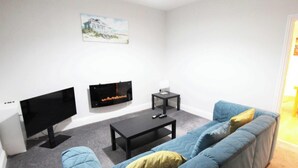 A living room with a flat-screen TV, a fireplace, a coffee table, and a blue sofa.
