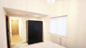 A bedroom with a bed, a wardrobe, a door leading to another room, and a window with blinds.