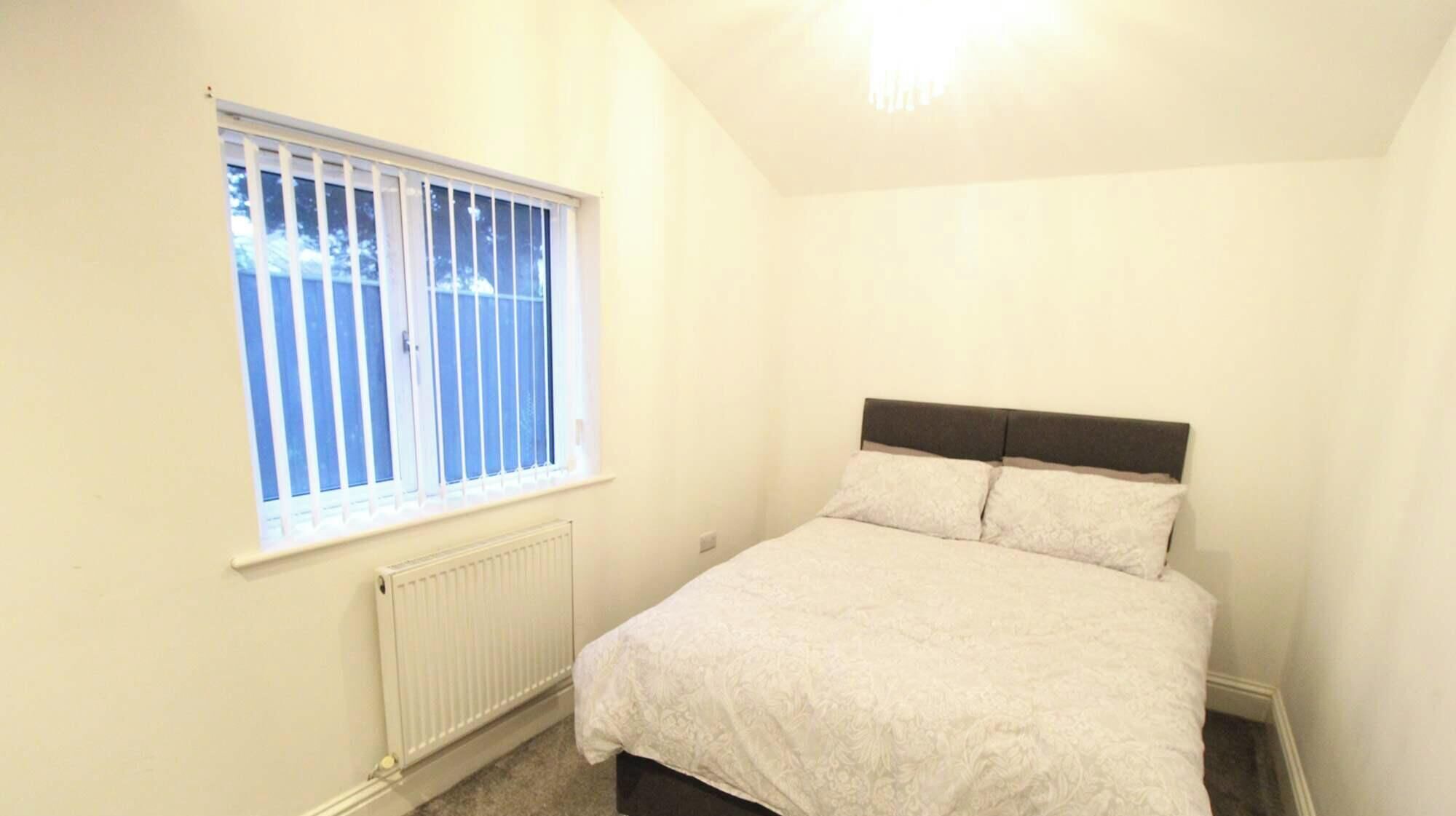 Une chambre avec un lit simple, une fenêtre avec des stores et un radiateur.