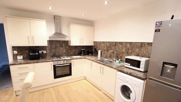 A modern kitchen with white cabinets, a gas stove, a microwave, a dishwasher, and a stainless steel refrigerator.