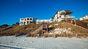 A beachfront property with a multi-level building, wooden stairs, and a sandy beach.