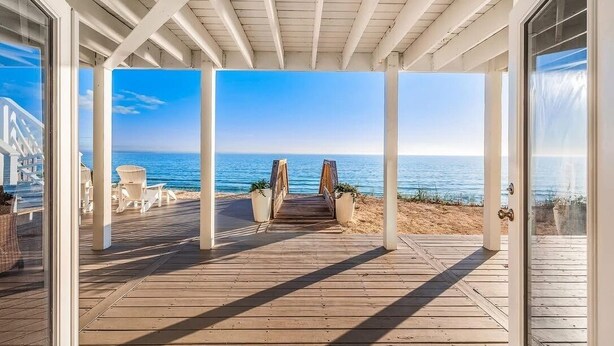 A wooden deck leading to a beach with a clear view of the ocean.