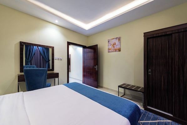 A hotel room with a bed, a desk, a chair, a wardrobe, and a door. - Al Qasr Hotel Suites -King Abdullah Road (Abha)