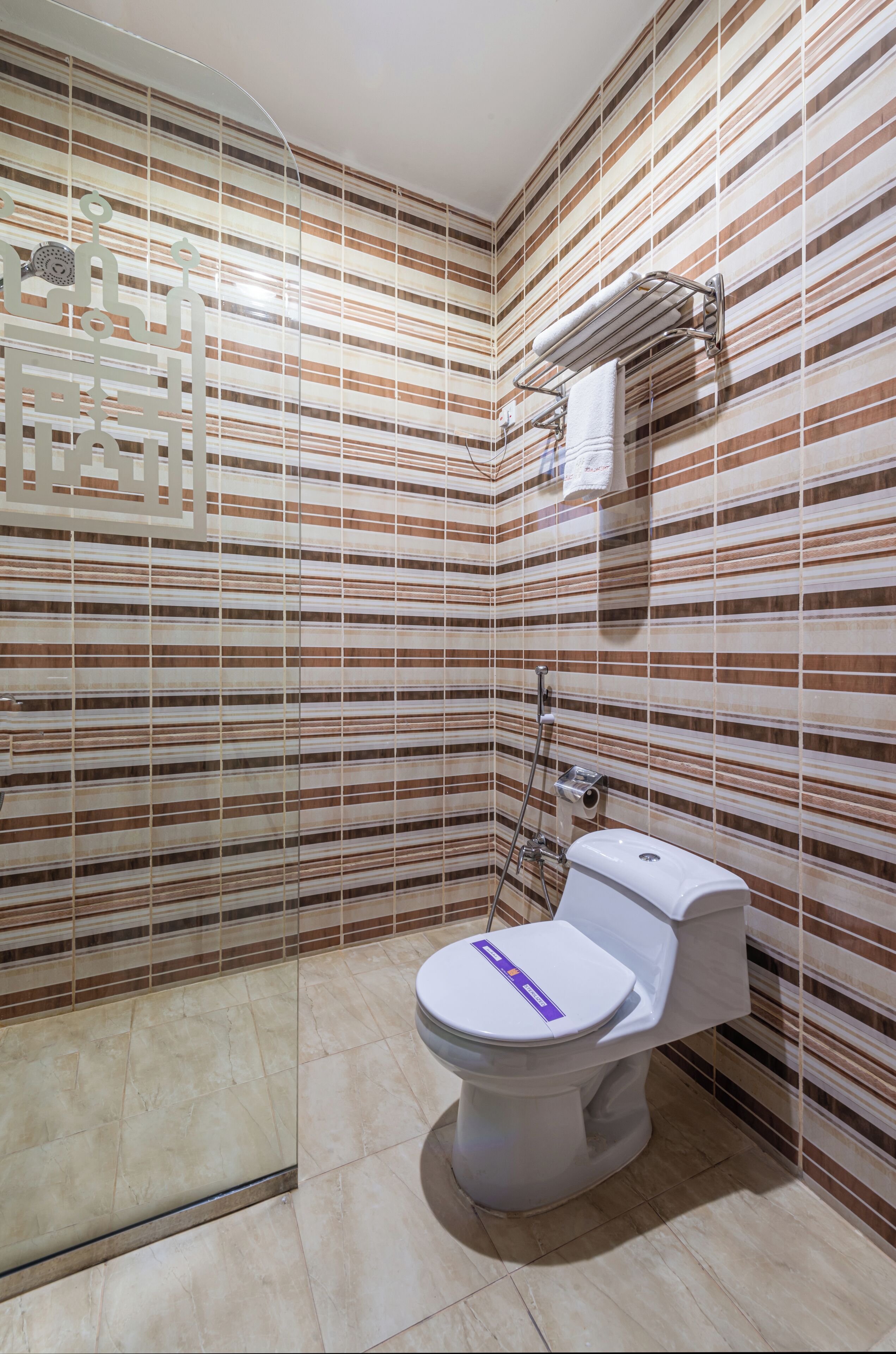 A bathroom with striped tile walls, a white toilet, and a shower area.