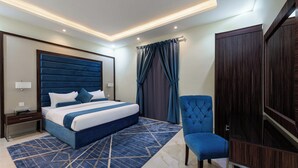 Une chambre d’hôtel moderne avec un grand lit, un fauteuil bleu rembourré, une armoire et un tapis à motifs.
