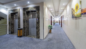 Un couloir d’hôtel aux murs de marbre, avec un tapis bleu et un tableau représentant des tournesols.