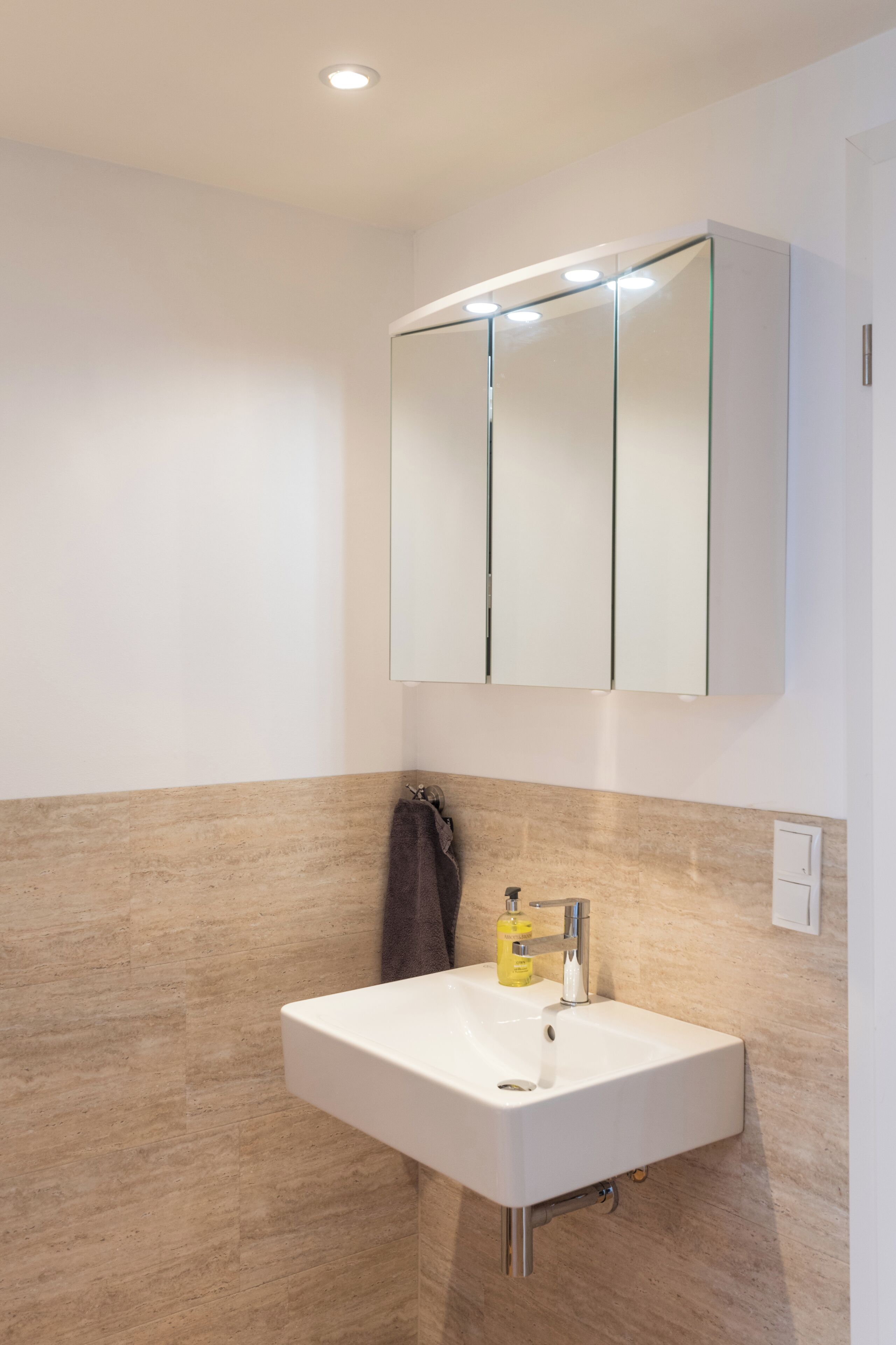 A bathroom with a white sink, a mirror cabinet, and beige tiled walls.