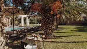 Un área de comedor al aire libre con una mesa lista para dos personas, rodeada de sillones de lounge y una palmera.