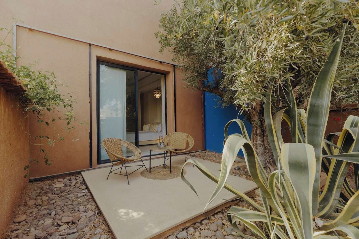 A modern outdoor seating area with two wicker chairs and a table, a large agave plant, and a building with a sliding glass door.