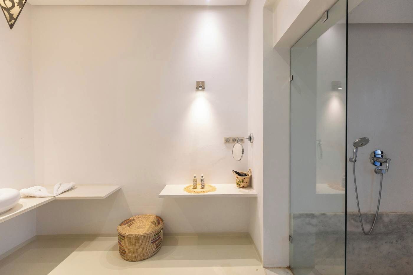 A modern bathroom with a glass shower enclosure, a white vanity with a towel, and a woven basket on the floor.