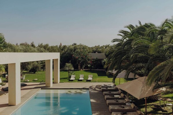 A pool area with lounge chairs and umbrellas, surrounded by greenery and palm trees.
