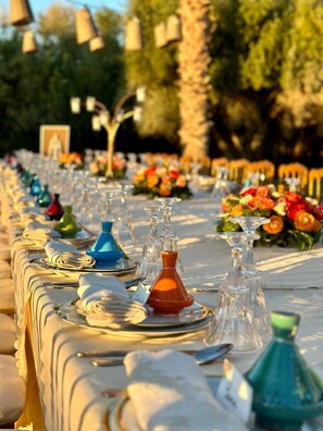 A long dining table set with plates, glasses, and napkins, surrounded by chairs and decorated with flowers.