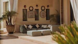 A modern outdoor seating area with a sofa and cushions, a large potted plant, and decorative wall art. - The Garden of Siredrah, an Oasis with Pool and Hammam (Marrakech)