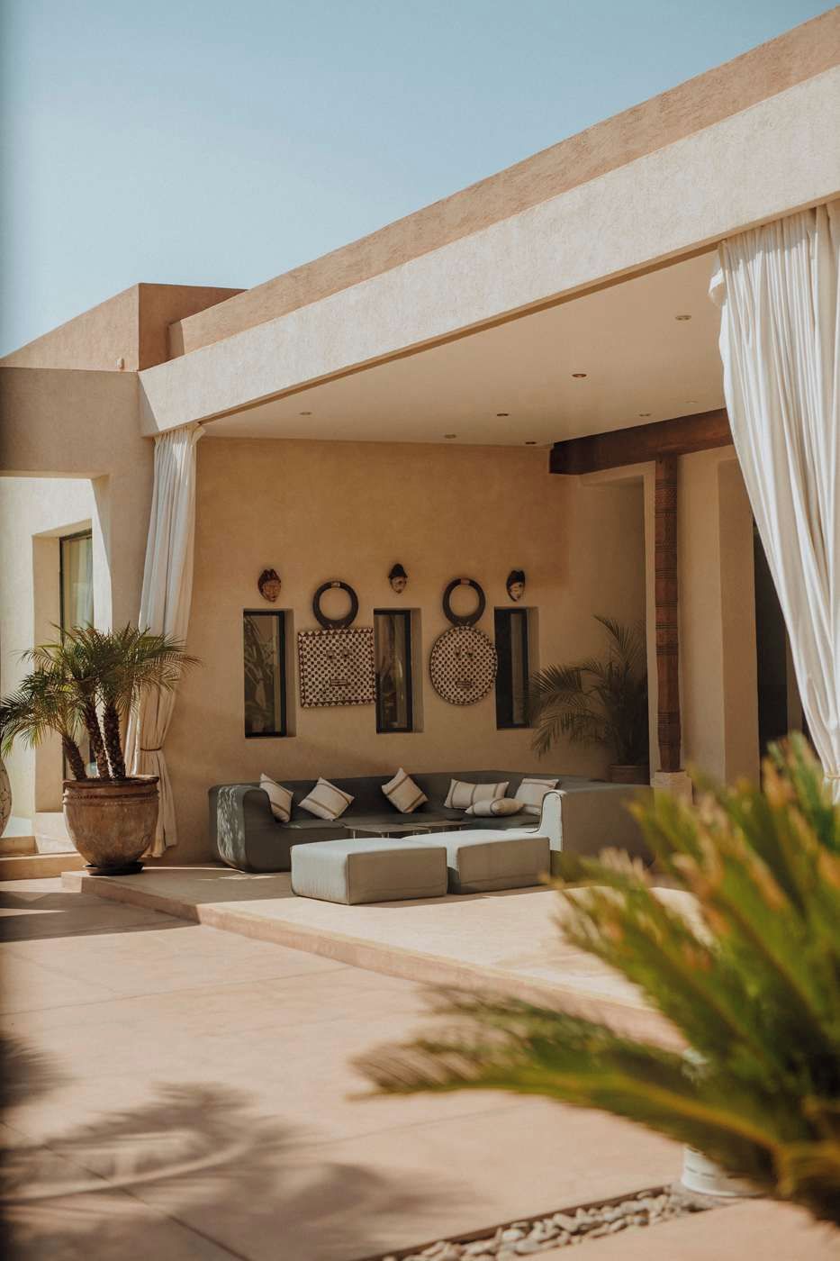 A modern outdoor seating area with a sofa and cushions, a large potted plant, and decorative wall art.