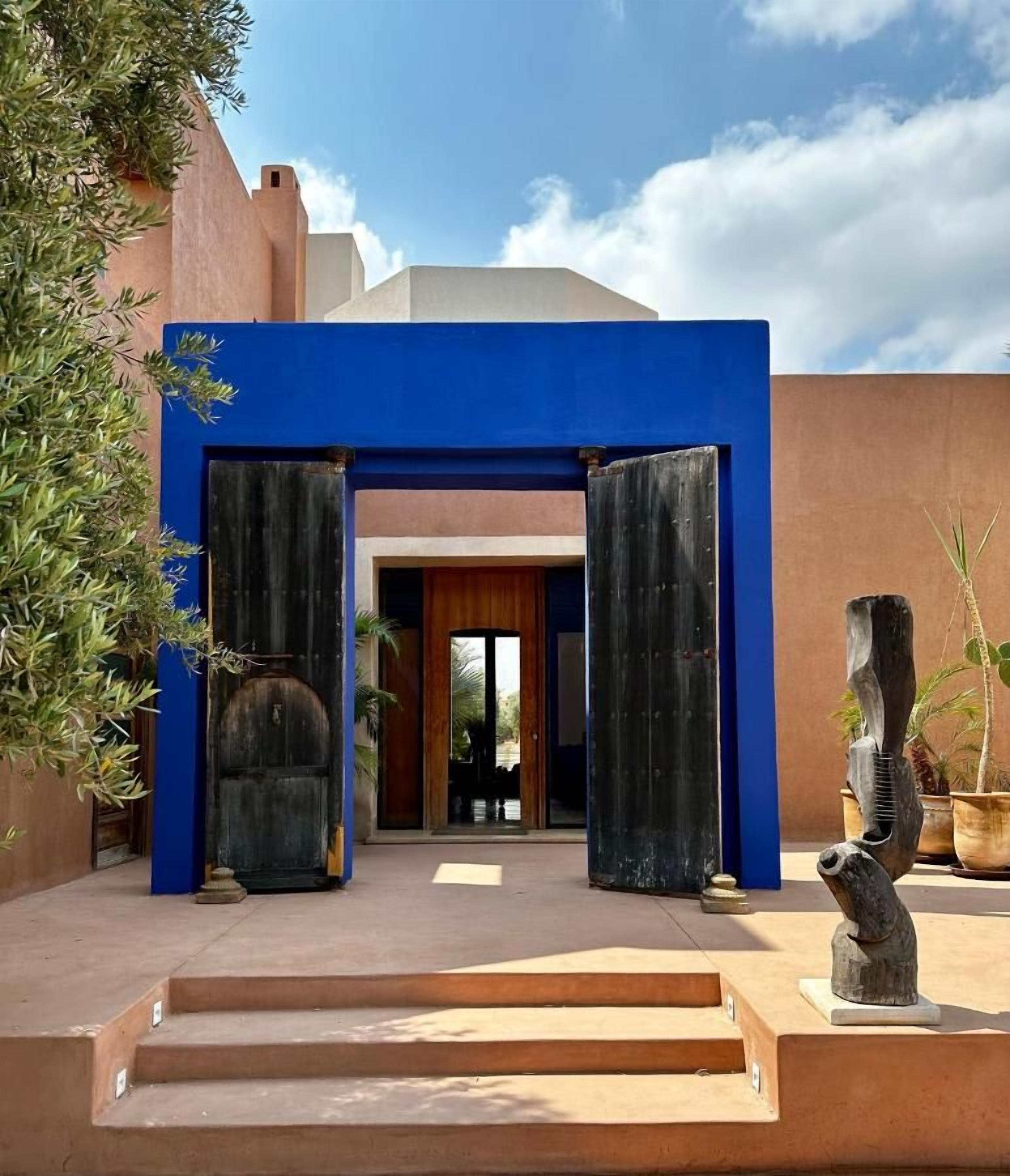 Entrada de un edificio con fachada azul, una puerta de madera y una escalera de hormigón que sube.