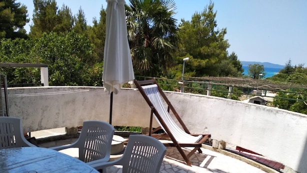 Um pátio com mesa e cadeiras, uma poltrona de descanso e vista para o mar.