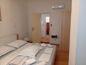 Ett sovrum med en säng, kuddar och prydligt hopvikta handdukar. Det finns en dörr som leder till ett annat rum, och en luftkonditioneringsenhet på väggen.