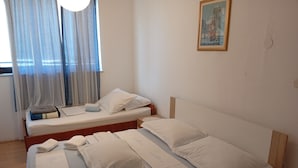 Quarto com duas camas, uma janela com cortinas estampadas, um quadro na parede, e toalhas e almofadas organizadas nas camas.