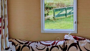 A room with a window overlooking a grassy area and a lighthouse.